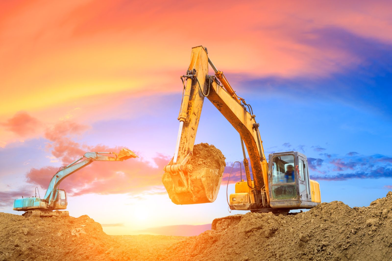 Two excavators work on construction site at sunset